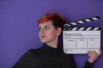 redhead woman holding movie  clapper on purple background