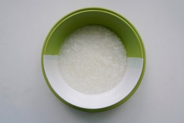 Top eye view closeups of congee, mush or boiled rice gruel asian style in circle half pastel green and white color bowl overlapped on green plate isolated on a white table background at a kitchen room