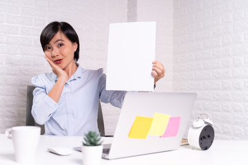 Happy woman sitting at home office and showing blank sheet