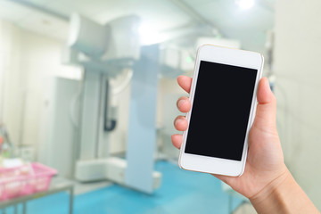 Smart phone with white screen in hand on blurred in X-ray room background