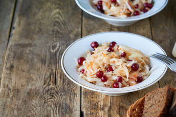 Sauerkraut with cranberries in a white bowl on wooden background
