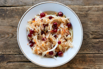 Sauerkraut with cranberries in a white bowl on wooden background 