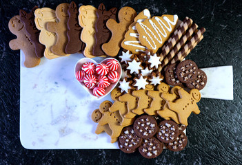 Happy Holidays Christmas large dessert grazing platter charcuterie board with gingerbread, chocolate and shortbread cookies with black and gold theme flat lay with negative copy space.