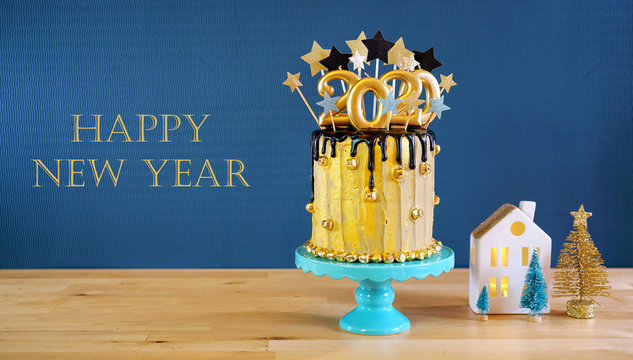Happy New Year's Eve 2020 black and gold drip cake on a modern stylish, festive, blue gold and white winter theme table setting with text greeting message.