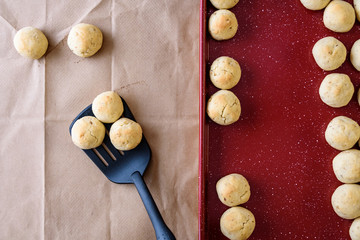 Fresh baked Russian Tea Cake cookies on a red non-stick baking sheet, brown paper for cooling baked cookies, black spatula