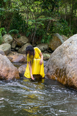 beautiful woman in yellow dress touching the river water