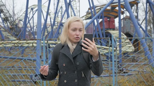 A woman blogger in a deserted abandoned amusement Park with a smartphone talking on video chat.