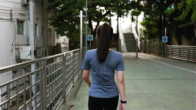 Back view young Asian woman athlete walking on the street after a run. Jogging workout lifestyle on the street at sunset. Healthy lifestyle.
