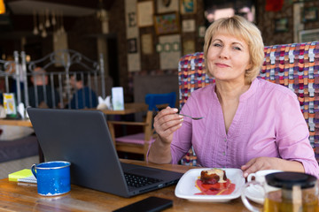 A woman with a laptop works in a cafe, she watches social networks.