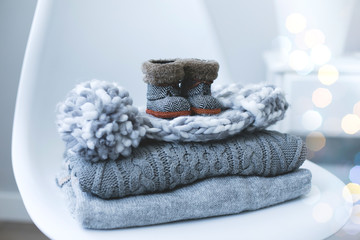 A stack of knitted sweaters, accessories and mini boots on chair in Interior of the living room