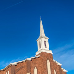 Fototapeta premium Square frame Sunny day view of a church with white steeple and vibrant blue sky background