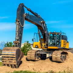 Square frame Close up of an excavator with arm bucket and continuous tracks on top of soil