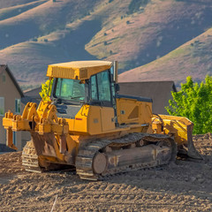 Square Yellow bulldozer on a construction site overlooking homes mountain and sky