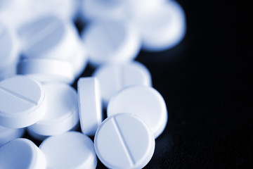White round pharmaceutical pills on a black surface close-up. Blue color toned