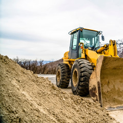 Square Front view of a yellow bulldozer against snow topped mountain and cloudy sky