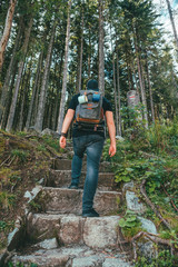 man with backpack walking by stone stairs that leads to the forest