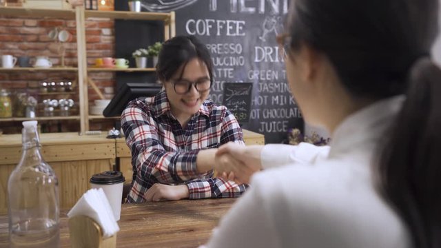 hr manager sitting at wooden table shaking hands with smiling girl job applicant after interview in coffeehouse. young woman applicant talking to human resource woman and handshaking in cafe store.