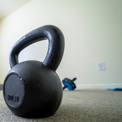 Fototapeta na wymiar Square Close up of black kettlebell inside a gym room with carpet floor and white wall