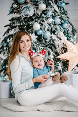 Obraz na płótnie Canvas Baby girl with mom on floor near Christmas tree. Happy New Year and Merry Christmas. Christmas decorated interior. The concept of family holiday.