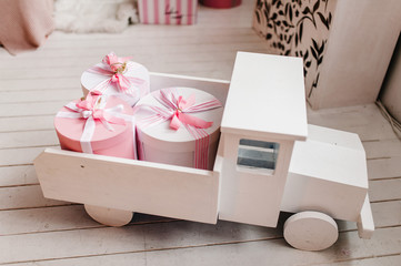 Toy white wooden car with gifts. Elegant pink boxes in back of truck. Birthday present. Copy space, holiday concept. Discounts, sale.