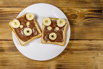Two sweet sandwiches with delicious chocolate hazelnut spread and banana in shape of bear on wooden table. Top view