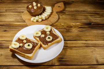 Obraz na płótnie Canvas Two sweet sandwiches with delicious chocolate hazelnut spread and banana in shape of bear on wooden table