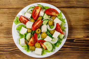 Greek salad with fresh vegetables, feta cheese and green olives on wooden table. Top view