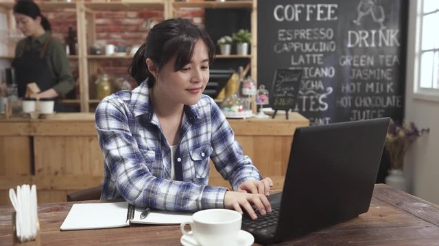 charming woman freelance worker sitting at table in cafe store writing in notebook and making note. female concentrated looking at laptop computer screen. girl barista working in counter coffee shop.