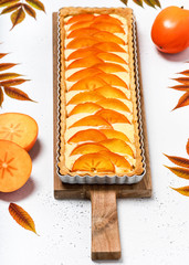 Sweet tart with persimmon and cream cheese on a wooden cutting board. Homemade food concept....