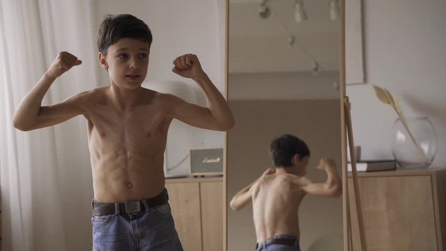 Cute caucasian boy showing muscles in front mirror, sport power, health care