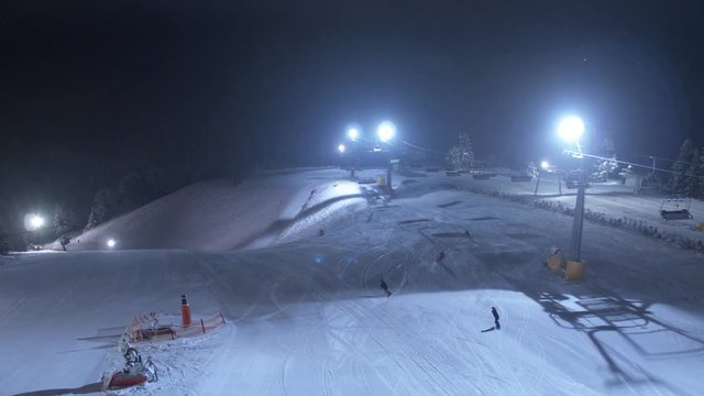 Drohnenaufnahme von einem Flutlicht beleuchteten Skigebiet, mit Skilift in einem Schneebedeckten Wald