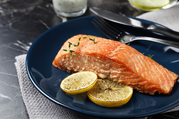 Tasty cooked red fish with lemon on dark marble table, closeup