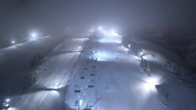 Drohnenaufnahme von einem Flutlicht beleuchteten Skigebiet, mit Skilift in einem Schneebedeckten Wald