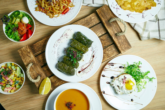 Dining table with a lot of dishes: dolama, vegetable salad, soup, beaf steak with egg and desserts. Top view, food flat lay