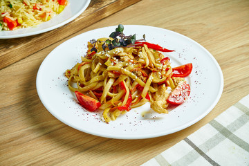 Pasta with tomatoes, bell pepper and chicken. Noodles with vegetables and meat on a white plate on a wooden background. Close up