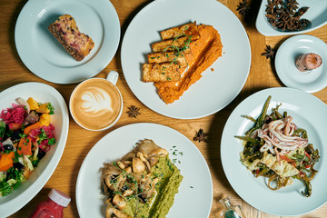 Dining table with a lot of dishes: fried tofu in curry, vegetable and Korean salad, coffee and desserts. Top view, food flat lay