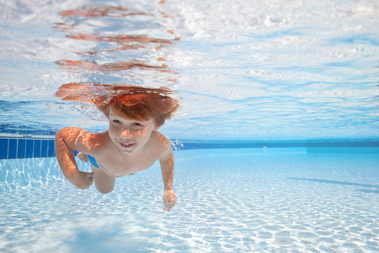 Happy young boy swim and dive underwater, kid breast stroke with fun in pool. Active healthy lifestyle, water sport activity and lessonson summer family vacation with child.