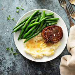 Traditional dinner meal with a bacon wrapped steak, green beans and mashed potatoes