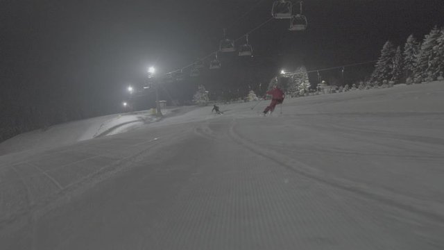 Skifahren auf einer mit Flutlicht beleuchteten Ski Piste, in einer weiten lowlight Aufnahme werden die Skifahrerinnen verfolgt