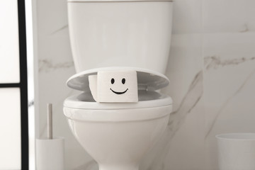 Roll of paper with funny face on toilet bowl in bathroom