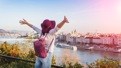 Fototapeta premium A happy young woman enjoying her trip to Budapest, Hungary from the point from Gellert Hill during sunrise in autumn during sunrise.