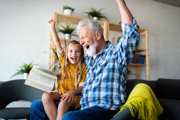 Bearded grandfather and his grandchild are having fun reading a book together - obrazy, fototapety, plakaty