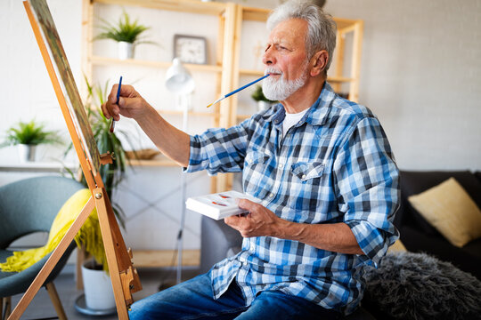 Smiling mature man painting on canvas at home