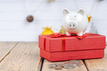 Piggy bank with coins and red gift box on wooden background. Festive and financial concepts