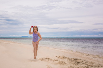 Fototapeta na wymiar Little girl in the rim in the form of Christmas trees and yellow swimsuit is standing on the beach