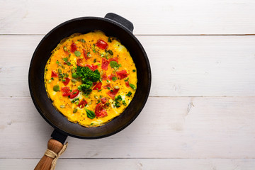 scrambled eggs with tomatoes in an old cast iron pan on a white wooden background with a copy space