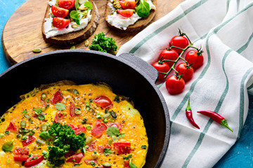 Healthy Breakfast on a cast iron pan. Scrambled eggs with greens and tomatoes, sandwiches with cream cheese, pesto and cherry tomatoes