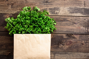 bunch of fresh greens, parsley in an eco-friendly paper bag on a wooden background with close-up copy space
