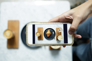 Female hand holding modern smartphone to takes photo of food