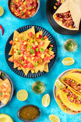 Mexican food, many dishes of the cuisine of Mexico, flat lay, top shot on a blue background. Nachos, tequila, taco shells, burritos, chili con carne